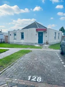 a white brick house with a blue door and a parking lot at Bungalowpark de Horn - 128 in Dirkshorn