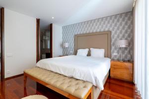 um quarto com uma grande cama branca e um banco em The Povoa Villa na Póvoa do Varzim
