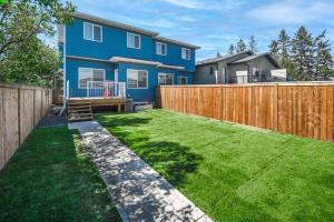 a backyard with a blue house and a wooden fence at Stay Together! 2 Family Units, Sleeps 16! FREE Banff Pass, Parking, Wine, BBQ, & Netflix! in Calgary
