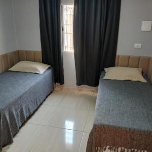 two beds sitting in a room with a window at Quarto Solteiro com TV in Artur Nogueira
