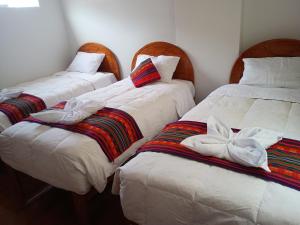 3 posti letto in una camera con lenzuola e cuscini bianchi di Hotel TIKA AYNA Cerca a la plaza de Armas CUSCO a Cuzco