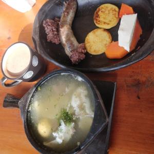 a table with a plate of food with a sausage and soup at Quinta las Marias, Ecolodge, camping y Tiny wood house in Guateque