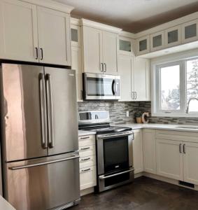 a kitchen with white cabinets and stainless steel appliances at Modern 3BR Near Airport & DT in Calgary