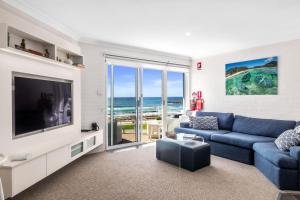Una sala de estar con un sofá azul y un televisor. en Mariners 5, en Mollymook