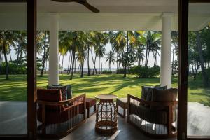 a porch with chairs and a table and palm trees at Kalkudah Beach House By Teardrop Hotels in Kalkudah