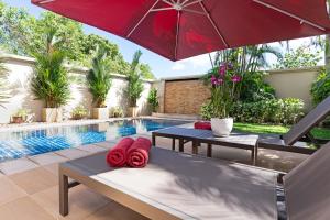 une piscine avec deux tables et un parasol rouge dans l'établissement The Residence Bangtao Villa 216, à Ban Thalat Choeng Thale