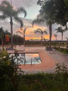 a swimming pool with palm trees and a sunset at Gite ECOPARADIS in Madagh
