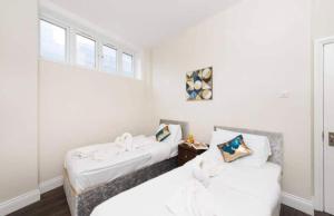two beds in a room with white walls and a window at Grand 2 Bed Apartment In London in Croydon