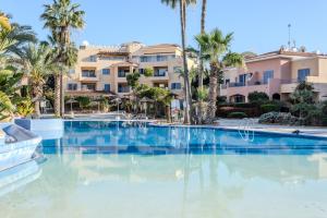 a large swimming pool with palm trees and condos at H&O Limnaria Elegance Pool View Apartment in Paphos City
