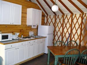 kuchnia z białymi szafkami, stołem i lodówką w obiekcie Yosemite Lakes Hillside Yurt 1 w mieście Harden Flat