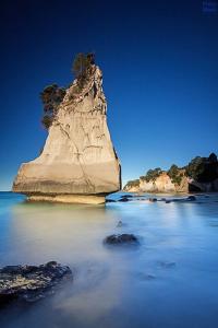 a large rock in the water next to a beach at Cathedral Cove Apartment in Hahei