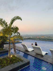 two people sitting on white chairs next to a swimming pool at Elegant 1BR with Great View, Panoramic Pool Near Ortigas CBD - 24 in Manila