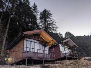 a wooden cabin with large windows in the woods at Navira Hills Kanatal in Kanatal