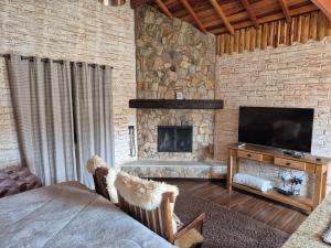 a bedroom with a stone wall with a television and a fireplace at Chalé Villa Magrini in Monte Verde
