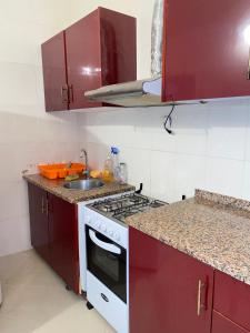 eine Küche mit roten Schränken, einem Herd und einer Spüle in der Unterkunft Mar Azul Tarrafal APARTMENT in Tarrafal
