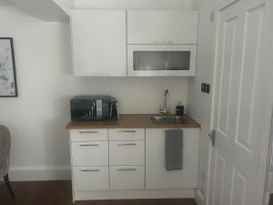 a kitchen with white cabinets and a sink and a microwave at Spacious studio with free EV recharge overnight in Watford