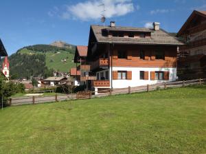 a large wooden house with a green field in front of it at Appartamenti Chedul in Selva di Val Gardena
