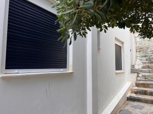 a window with black blinds on a white building at Sufiko Studios - Drosia in Armenistis