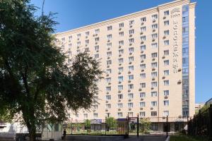 a large white building with a tree in front of it at One Bedroom Apartment Near Arbat In The Golden Square of Almaty in Almaty