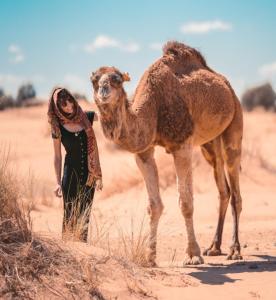a woman standing next to a camel in the desert at Dar Menorca in Merzouga