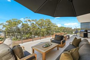 an outdoor patio with couches and tables and an umbrella at Oceanview Penthouse by Experience Jervis Bay in Huskisson