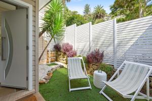 two white chairs sitting in a yard next to a fence at Luxury 2-Bed with Ocean Views and Garden in Collaroy