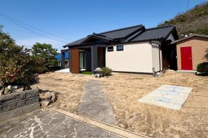 a house with a red door and a yard at My Place 小豆島 1日1組限定 海近の贅沢ステイ 2025年フルリノベ 洗練モダンデザイン 最大8名 一棟貸切 in Tonosho