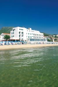 a beach with a large white building and the water at Hotel Amyclae in Sperlonga