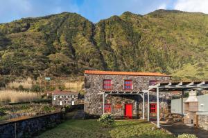 a stone house with red doors in front of a mountain at Kuanza Nature Experience, Fajã do Belo in Fajã da Caldeira de Santo Cristo