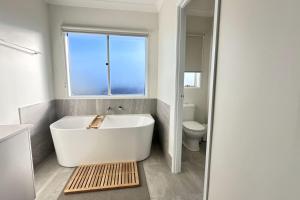 een witte badkamer met een bad en een raam bij Lotus Grand Home in Mango Hill Sleeps 8 in North Lakes +24 foto's