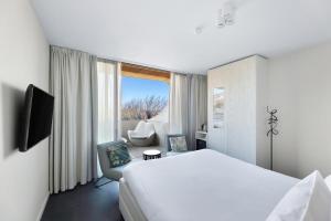 a white hotel room with a bed and a chair at Duinhotel Tien Torens in Zoutelande