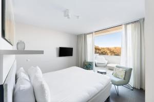 a white bedroom with a white bed and a window at Duinhotel Tien Torens in Zoutelande