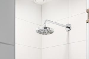 a shower with a shower head on a white tile wall at Duinhotel Tien Torens in Zoutelande