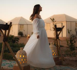 Uma mulher de vestido branco em pé em frente a tendas. em Merzouga Luxury Glamping em Merzouga