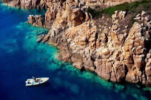 a boat in the water next to a rocky cliff at Chia Laguna - Hotel Village in Chia