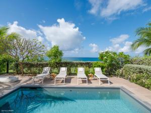 a pool with chairs and the ocean in the background at Chez Paulette à distance à pied de la plage et piscine chauffée in Friar's Bay