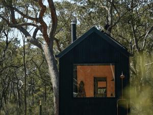 a black tiny house next to a tree at Secluded Forest Cabin with No Reception - Alon in Kulnura