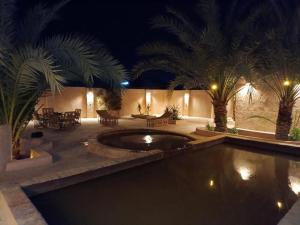 a swimming pool with palm trees in a backyard at night at Tulip Camp Siwa Oasis in Siwa