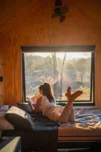 Una mujer tendida en una cama mirando por la ventana en Secluded & Pet Friendly Cabin Deep in Nature - Remy, en Coleyville