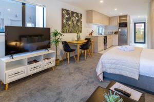 a bedroom with a bed and a television and a kitchen at Modern Studio Retreat Prime City Fringe Location in Christchurch