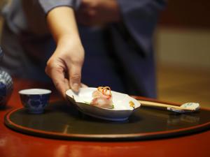 eine Person, die eine Schüssel Essen auf einem Tisch hält in der Unterkunft Kinjohro in Kanazawa