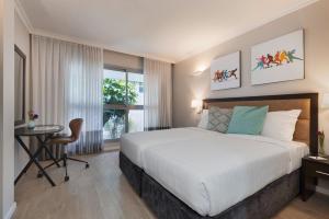 a bedroom with a bed and a desk and a window at Kfar Maccabiah Business & Sport Hotel in Ramat Gan