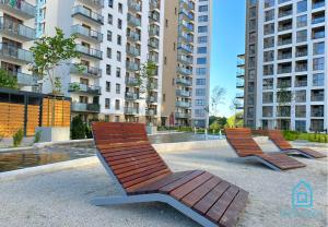 グダニスクにあるCoast Apartment with Sauna & Gym, 5 Min to Baltic Sea & Polsat Plus Arenaの高層ビルのある公園にある2つの木製ベンチ