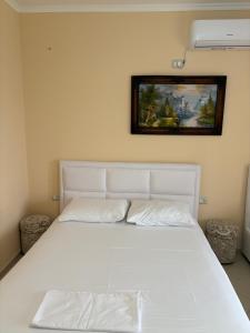 a white bed in a bedroom with a painting on the wall at STEFAN VASILI in Sarandë