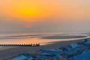 a sunset over a beach with a pier and the ocean at Willow Way 169 - Camber Sands in Camber