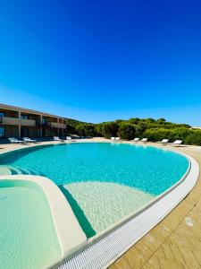 a large swimming pool with chairs and blue water at Rocce Rosse Isola Rossa in Isola Rossa