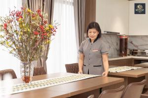 a woman standing next to a table with flowers at Khách sạn MoonLight An Khánh Hà Nội in Vân Lũng