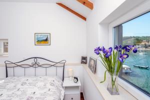 a bedroom with a bed and a window with purple flowers in a vase at Apartment Island Oasis in Koločep