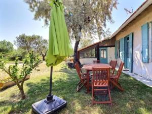 a patio table with a green umbrella on the grass at Charmante maison en Camargue avec piscine partagée in Saintes-Maries-de-la-Mer