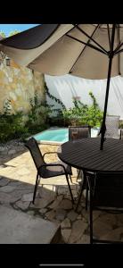 a table and chairs with an umbrella and a pool at Villa Mykonos - Experiência Grega Exclusiva em Tiradentes - 5 Suítes de Luxo in Tiradentes